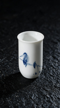 Tall white tea cup with a cobalt-blue bird perched on a leafy branch